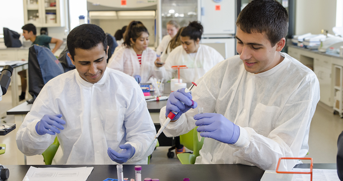 Students in lab gear using pipettes and test tubes