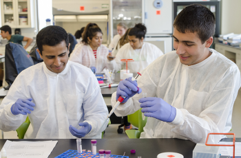 Students in lab gear using pipettes and test tubes